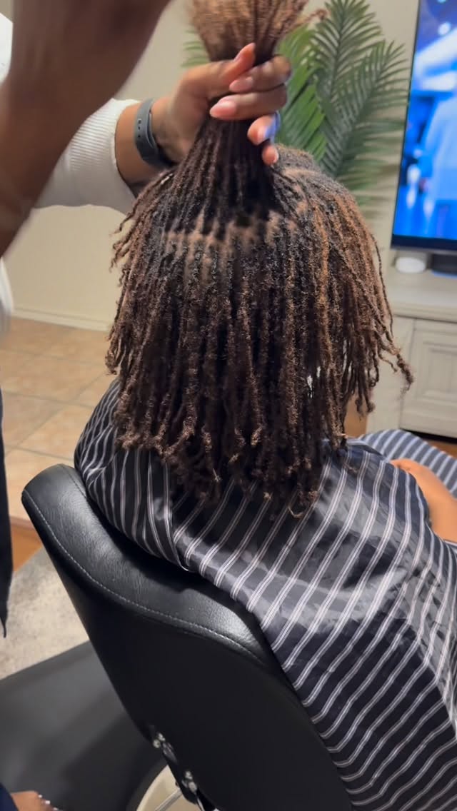 Person with medium-length dreadlocks sitting in a barber chair.